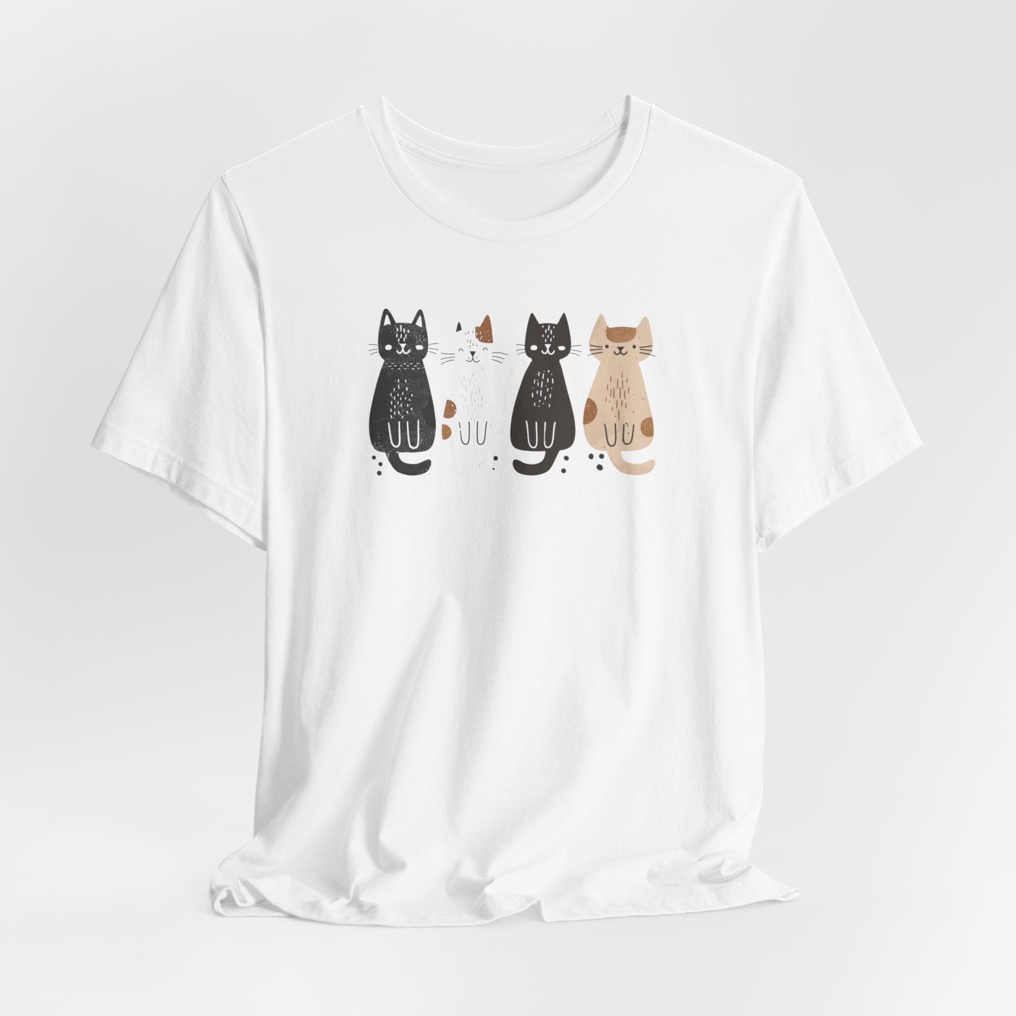 A white t-shirt featuring a graphic design of four cute cats in a lineup, each in different colors such as black, white, brown, and tan.