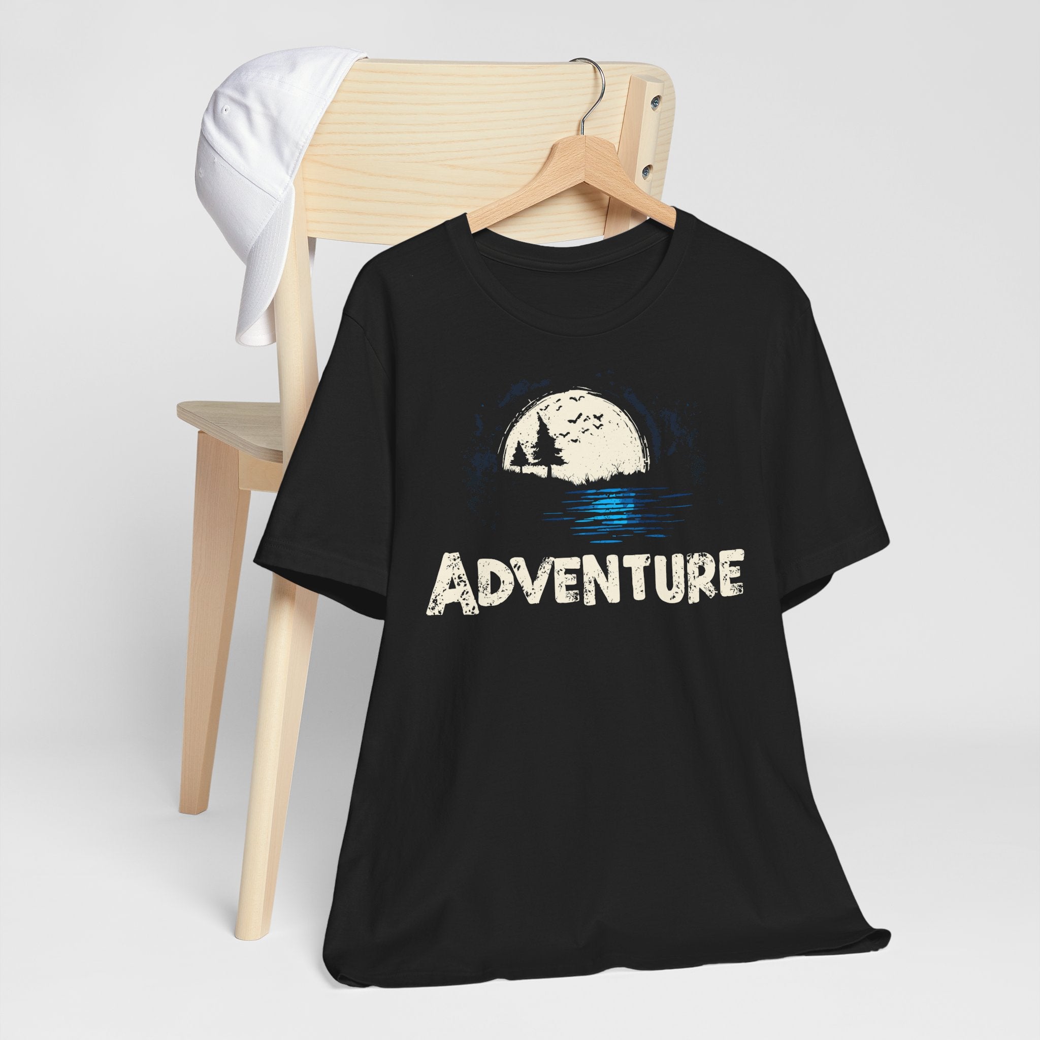 Black t-shirt with 'ADVENTURE' graphic on a wooden chair against a white background