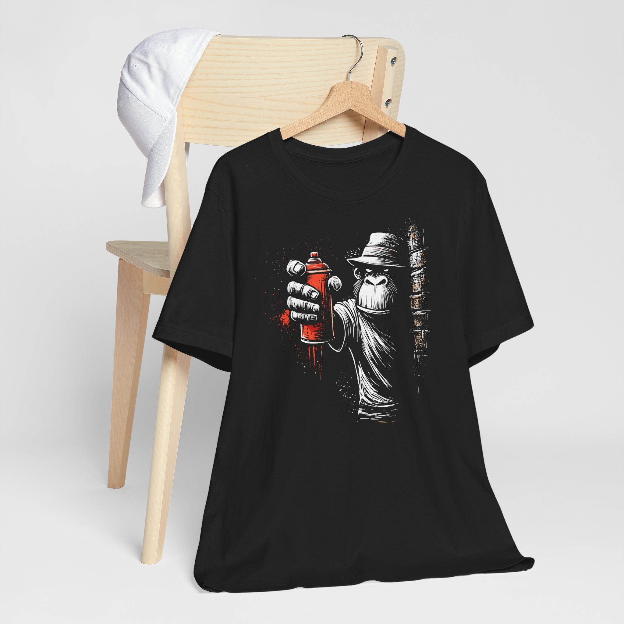 Black t-shirt with graphic design of a hand holding a spray can, hanging on a wooden chair.