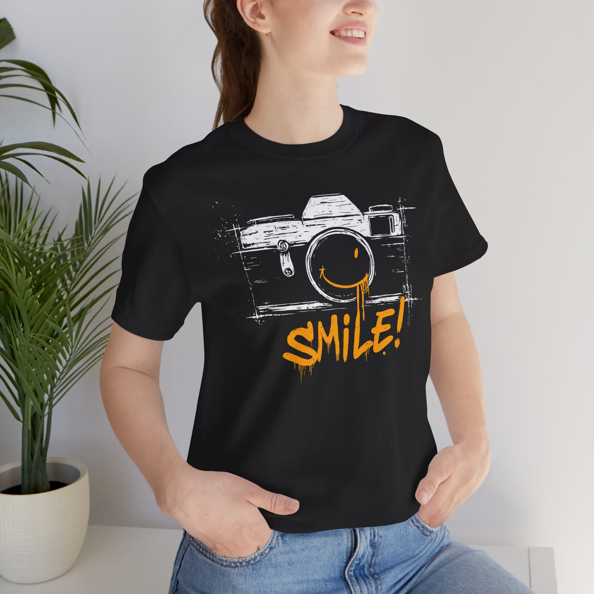 Person wearing a black t-shirt with a camera graphic and 'SMILE!' text, standing indoors.