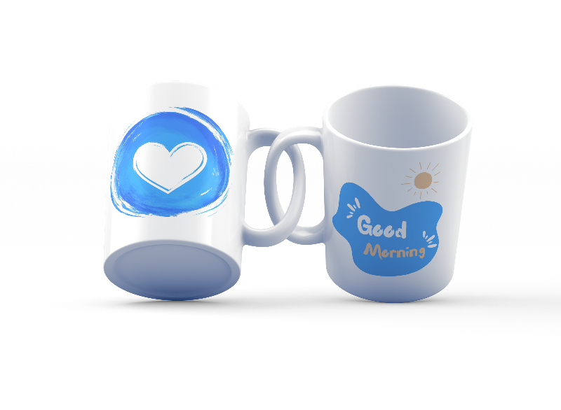 Two ceramic coffee mugs, one with a blue heart design and the other with a 'Good Morning' message alongside a sun icon, both with white backgrounds.