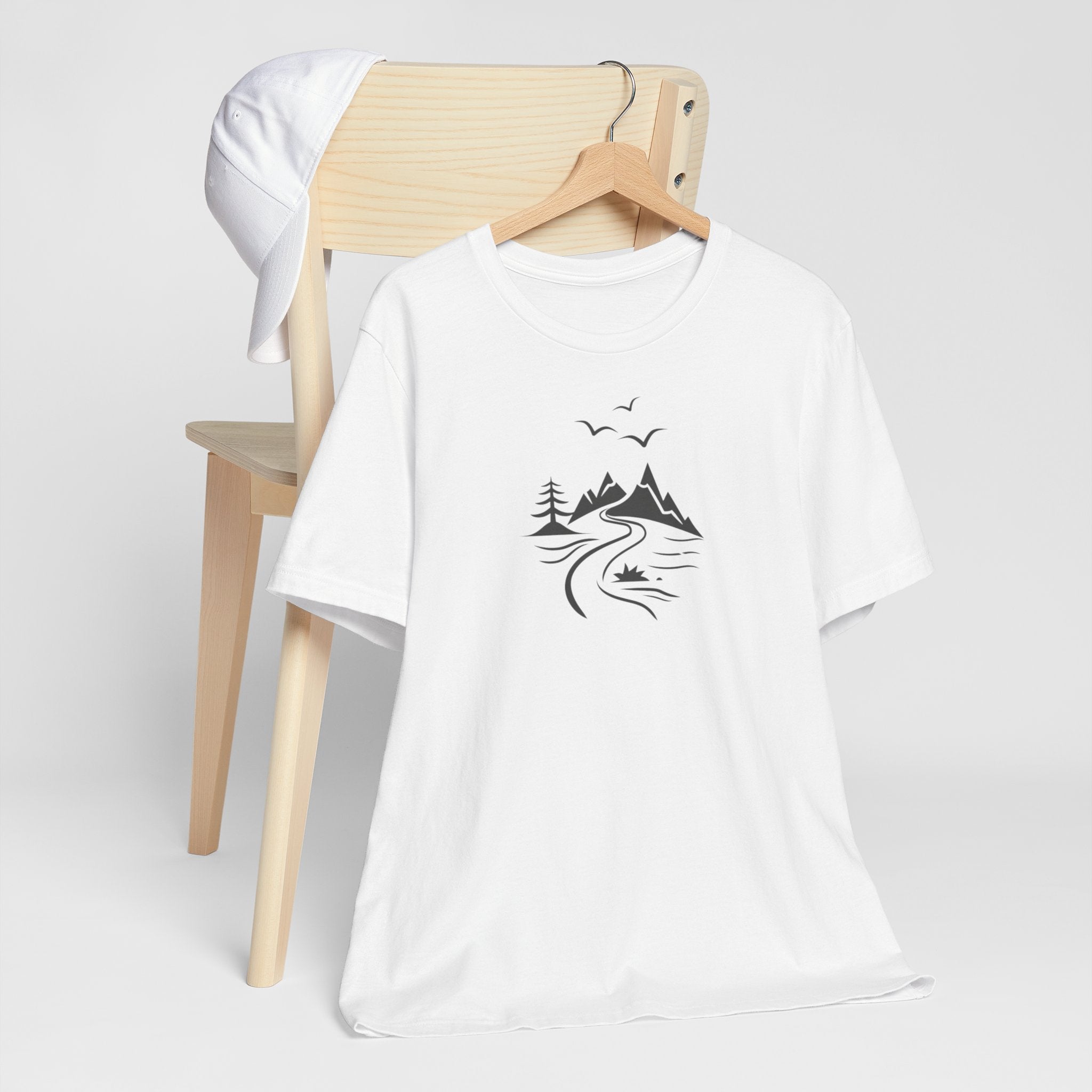 A white t-shirt featuring a minimalist black-and-white illustration of a mountain range, a river, and birds.