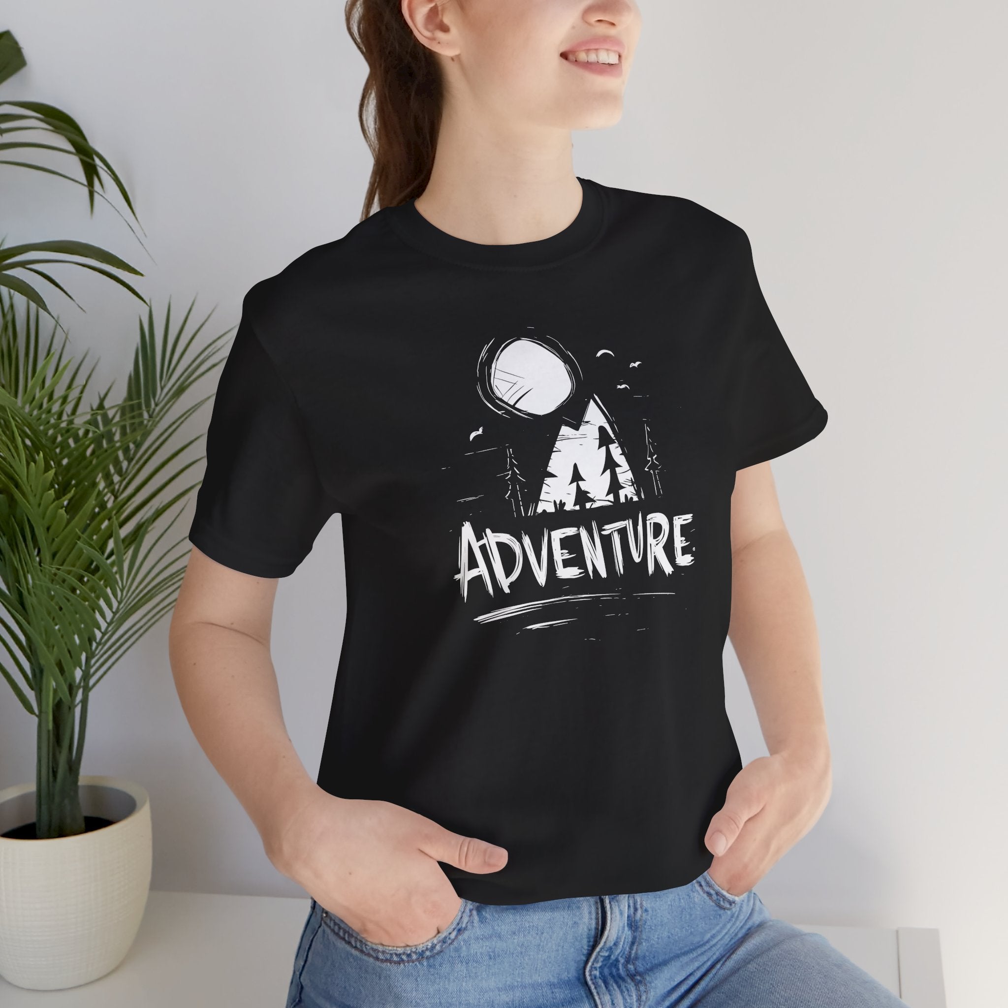Person wearing a black t-shirt with 'ADVENTURE' and mountain graphic, standing indoors.