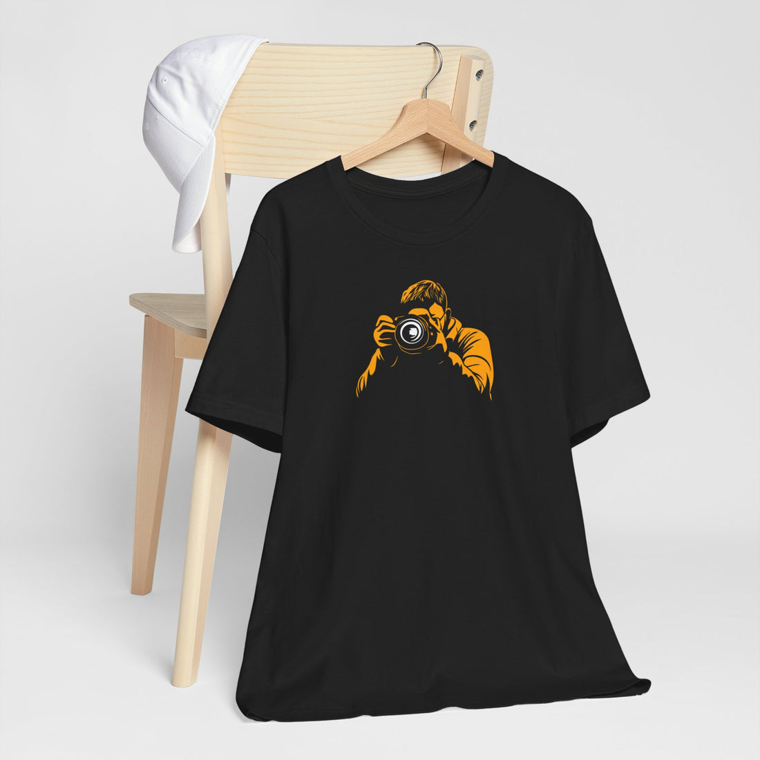 A black crew neck t-shirt with a bold yellow graphic of a photographer holding a camera.