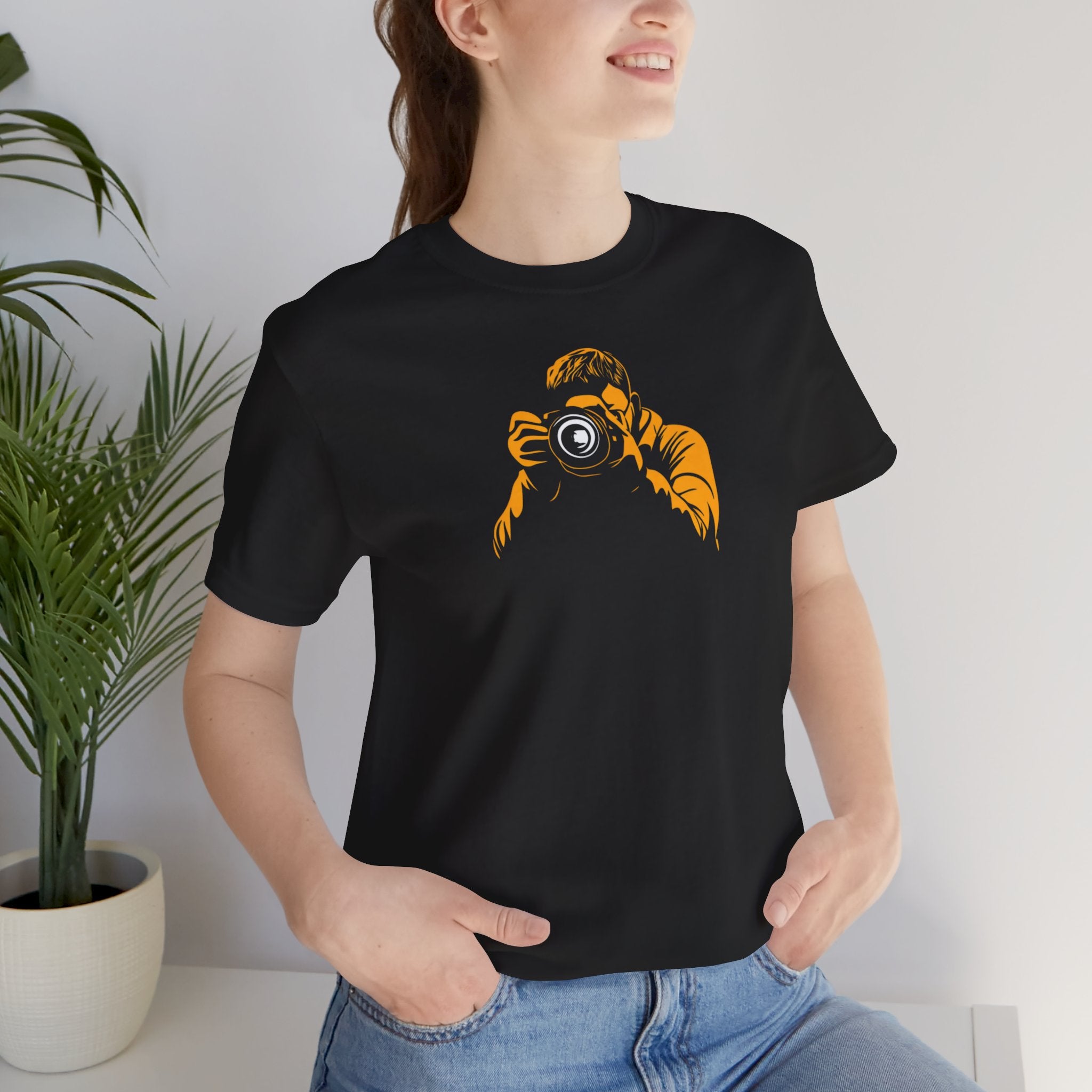 A black crew neck t-shirt with a bold yellow graphic of a photographer holding a camera.