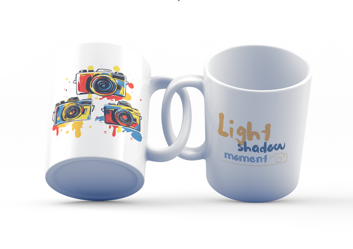 Two white ceramic mugs with colorful camera collage design and the quote 'Pictures Speak More'. One mug shows the exterior with a handle on the right side, and the other displays the interior with a blue color at the bottom.