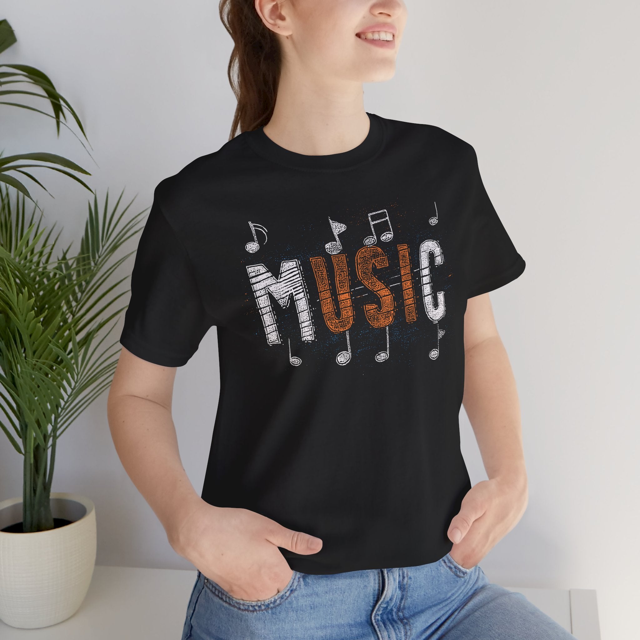 Person wearing a black t-shirt with 'MUSIC' and musical notes design, standing indoors.