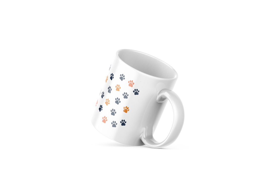 A ceramic coffee mug with a design of a cat face on one side and blue paw prints on the other, against a white background.