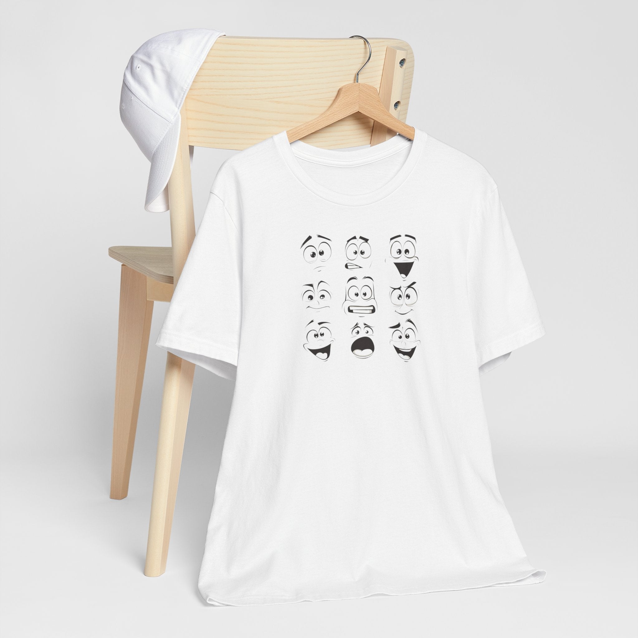 A white cotton unisex t-shirt featuring a design of various expressive cartoon faces.
