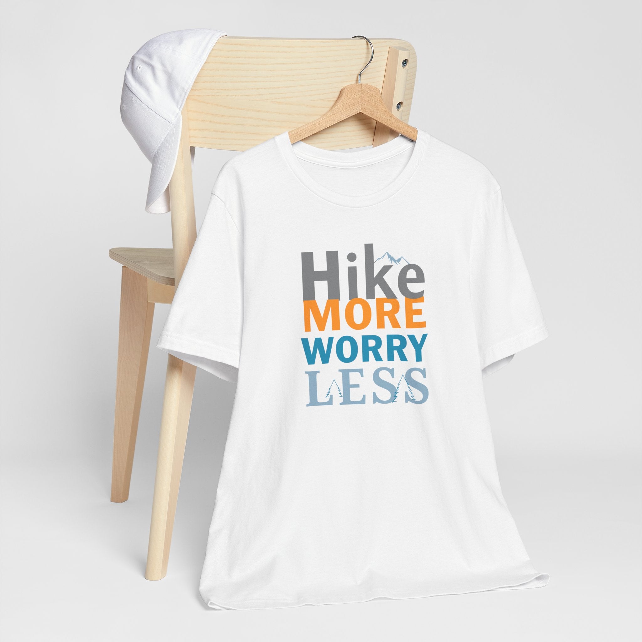 White crew neck t-shirt with the text 'Hike More Worry Less' printed in a gradient of orange, gray, and blue.