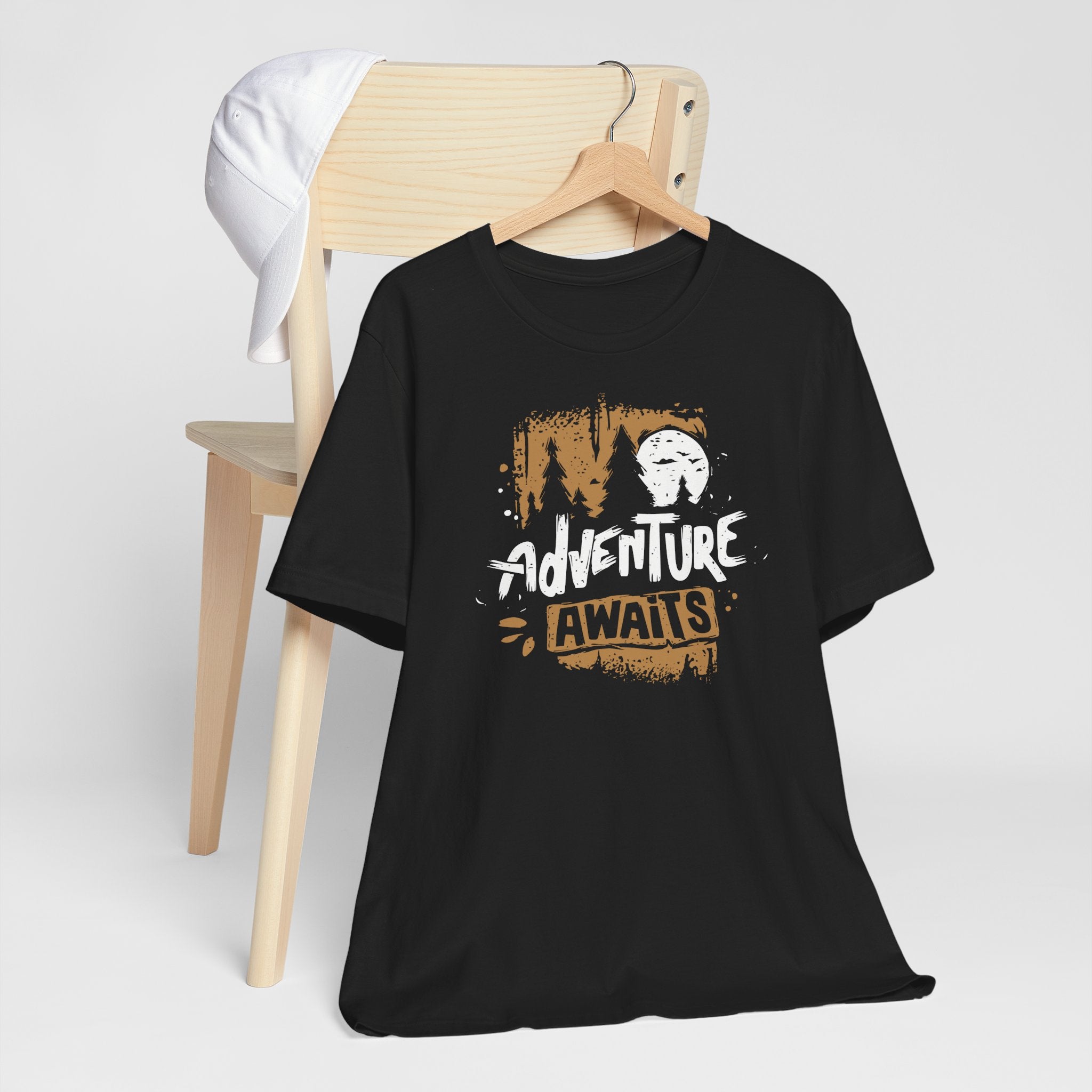 Black t-shirt with 'Adventure Awaits' graphic on a wooden chair against a white background