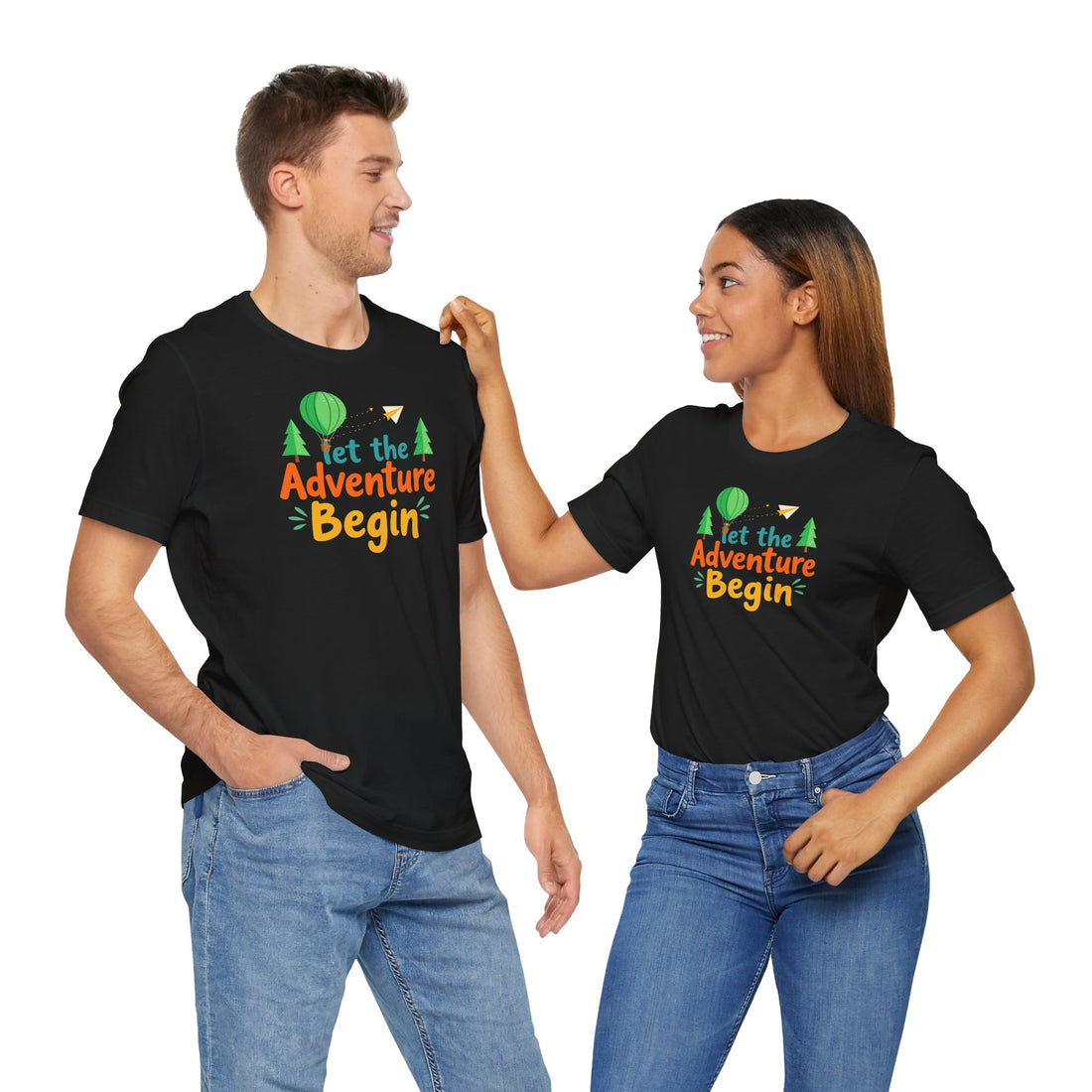 A black crew neck t-shirt with the phrase 'Let the Adventure Begin' printed in a colorful font, accompanied by images of a hot air balloon, trees, and a paper plane.