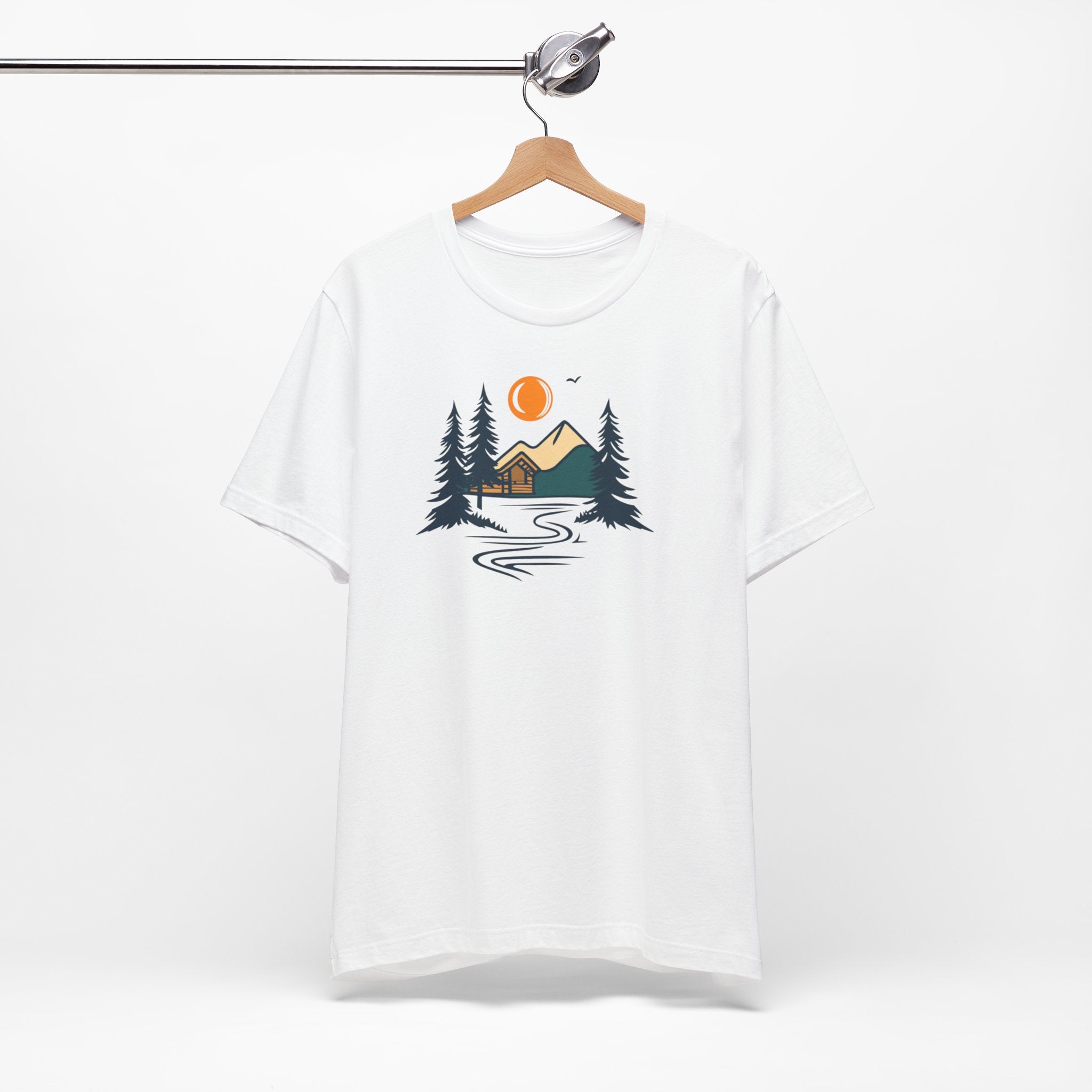 A white cotton t-shirt with a graphic design featuring a cabin, trees, and a mountain range with a warm orange sun.