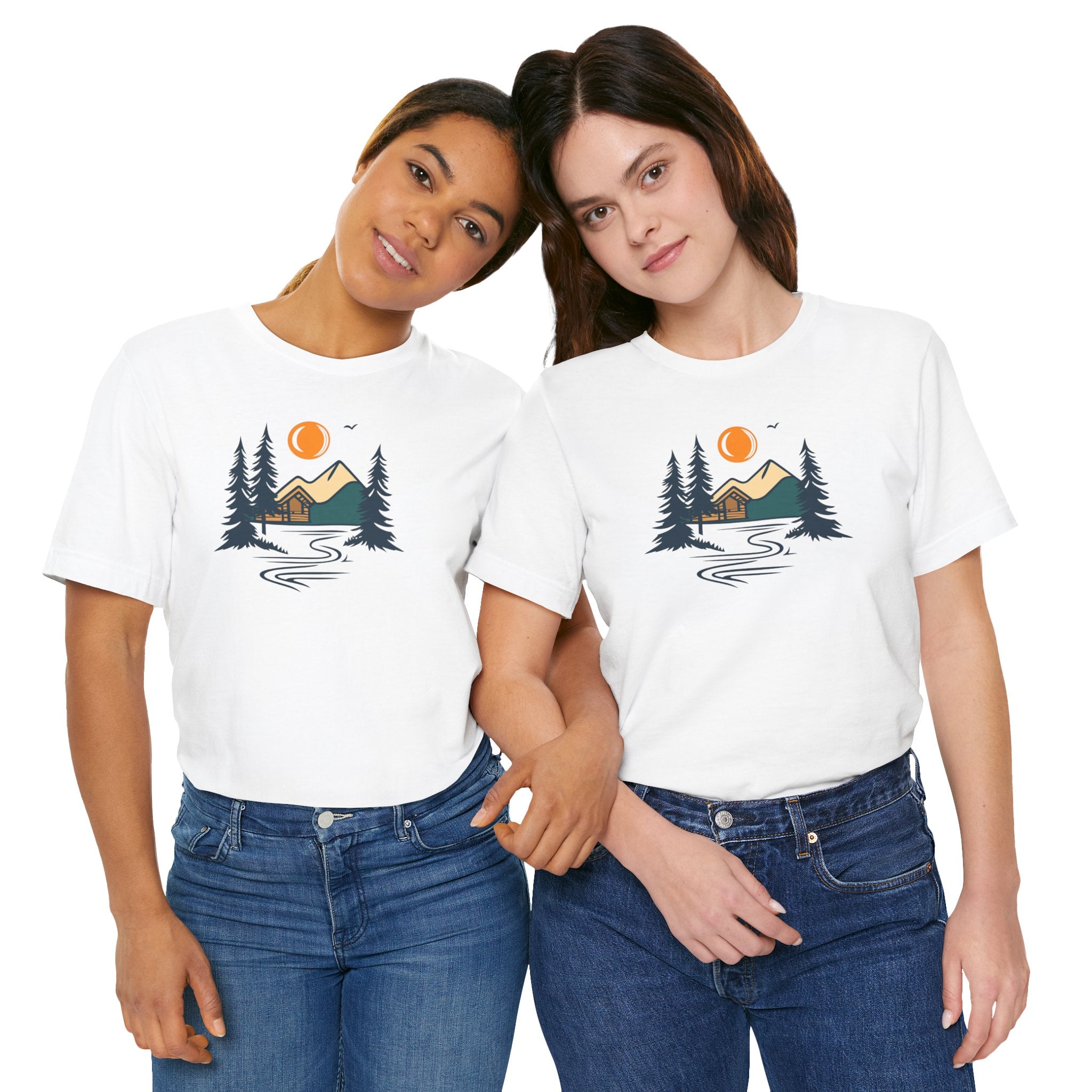 A white cotton t-shirt with a graphic design featuring a cabin, trees, and a mountain range with a warm orange sun.