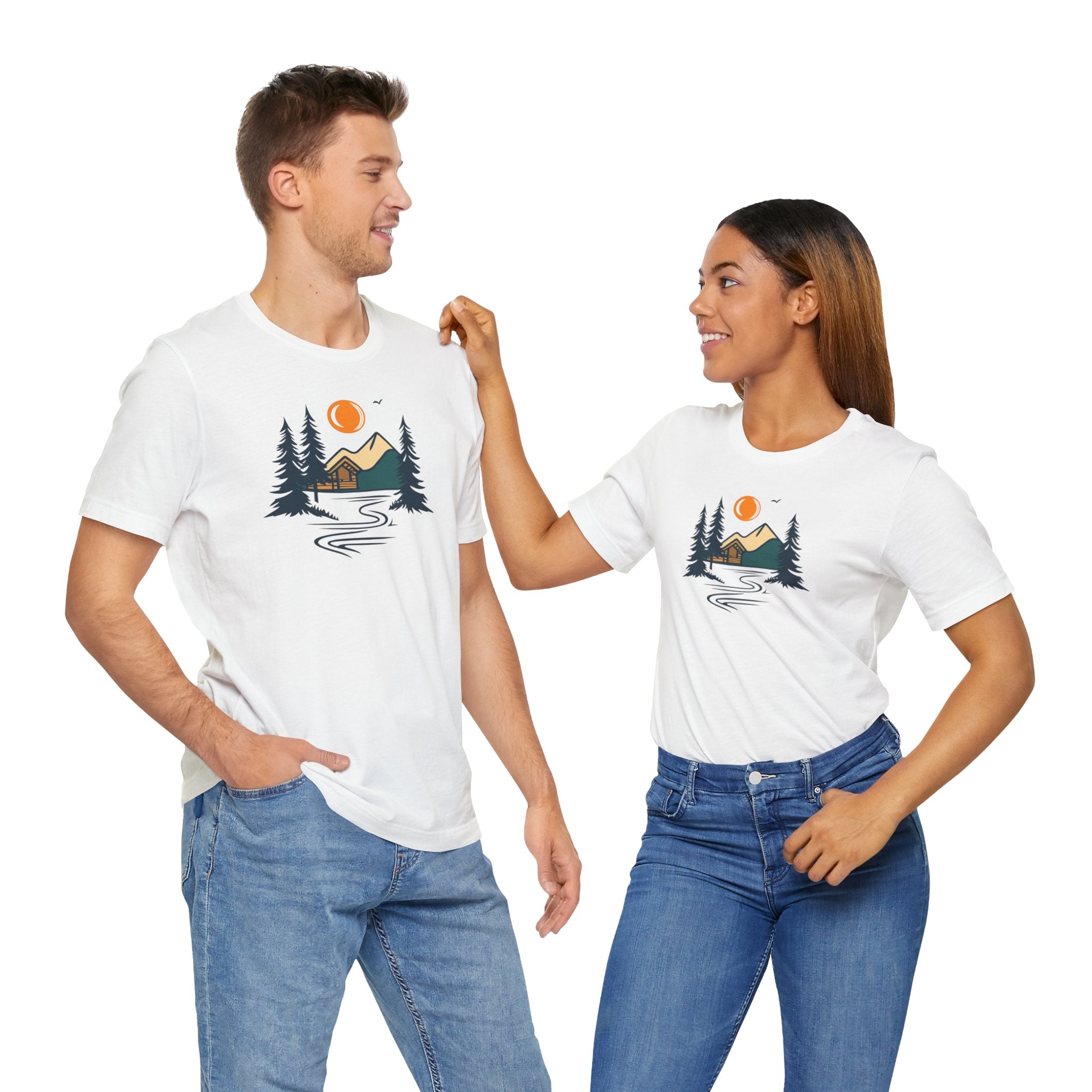 A white cotton t-shirt with a graphic design featuring a cabin, trees, and a mountain range with a warm orange sun.