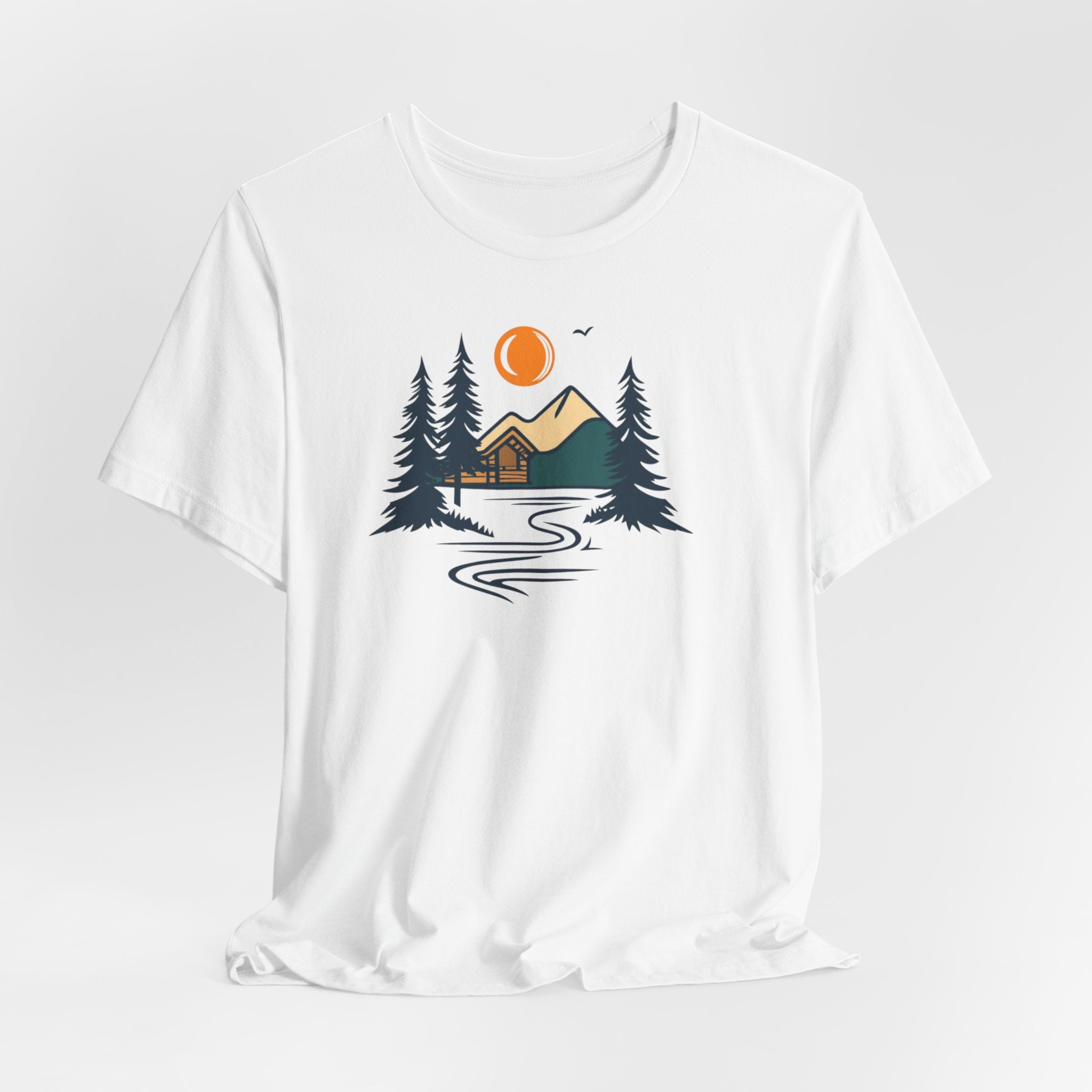 A white cotton t-shirt with a graphic design featuring a cabin, trees, and a mountain range with a warm orange sun.