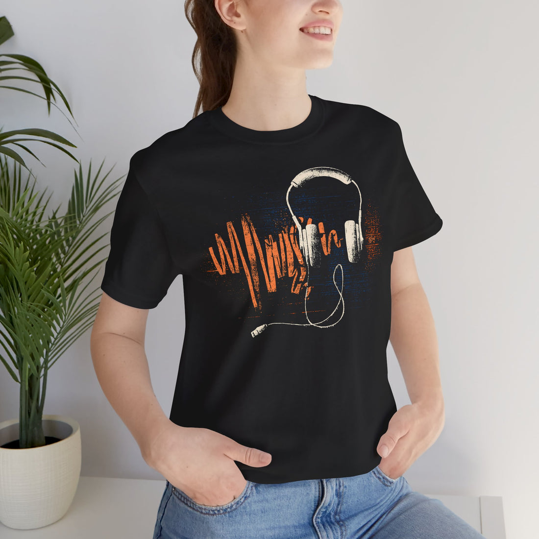 Person wearing a black t-shirt with a graphic design of headphones and text, standing indoors.