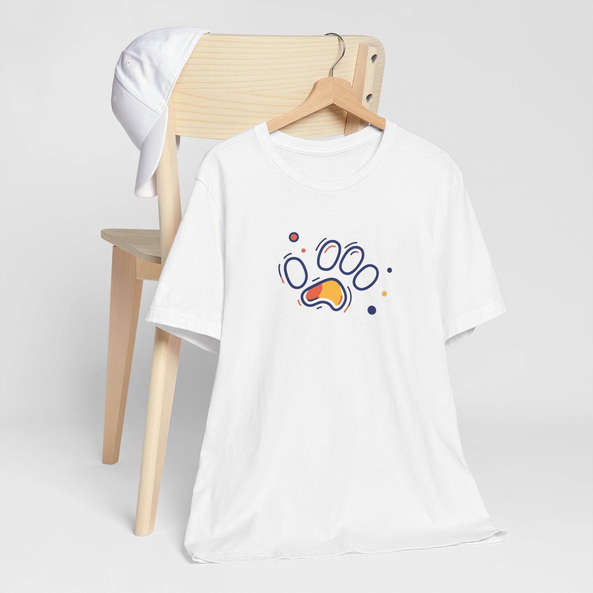 A white cotton t-shirt featuring a vibrant geometric paw print design in orange and navy tones, with abstract shapes.