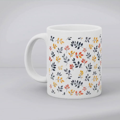 A set of two ceramic coffee mugs with a floral and autumn leaf design on a white background, one mug is filled with a liquid, possibly coffee or tea.