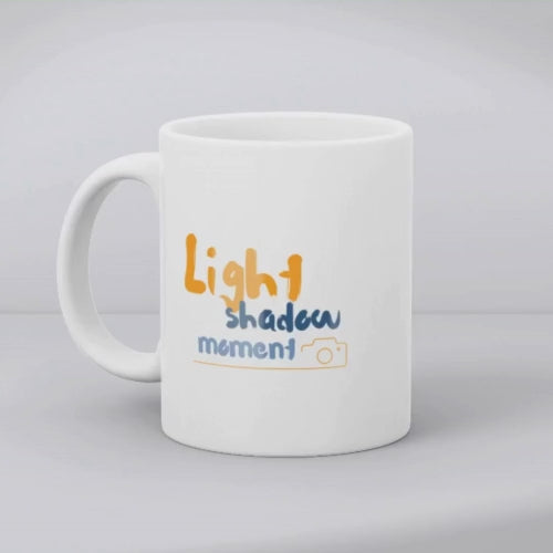 Two ceramic mugs, one with a colorful retro camera collage design and the text 'Light, Shadow, Moment!' The other mug is plain white with no design.