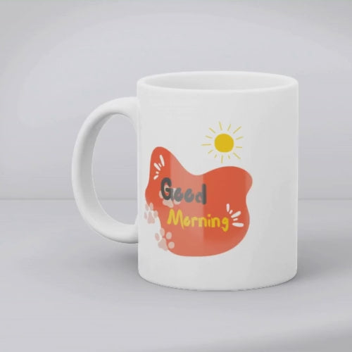 A double-sided ceramic coffee mug with an orange paw print design and 'Good Morning' message on one side, and a plain background on the other.