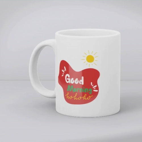 Two ceramic coffee mugs with festive Christmas designs. One mug has a reindeer with a Santa hat and 'Merry Christmas' text, and the other mug has a sun with 'Good Morning Ho Ho Ho' text.