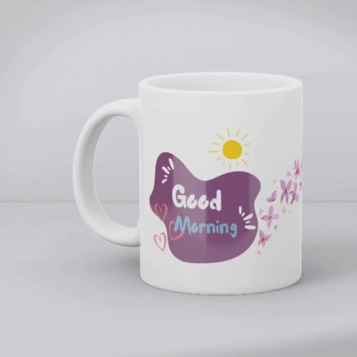 A ceramic coffee cup with a pink butterfly and hearts design, and a text message that reads 'Good Morning'.
