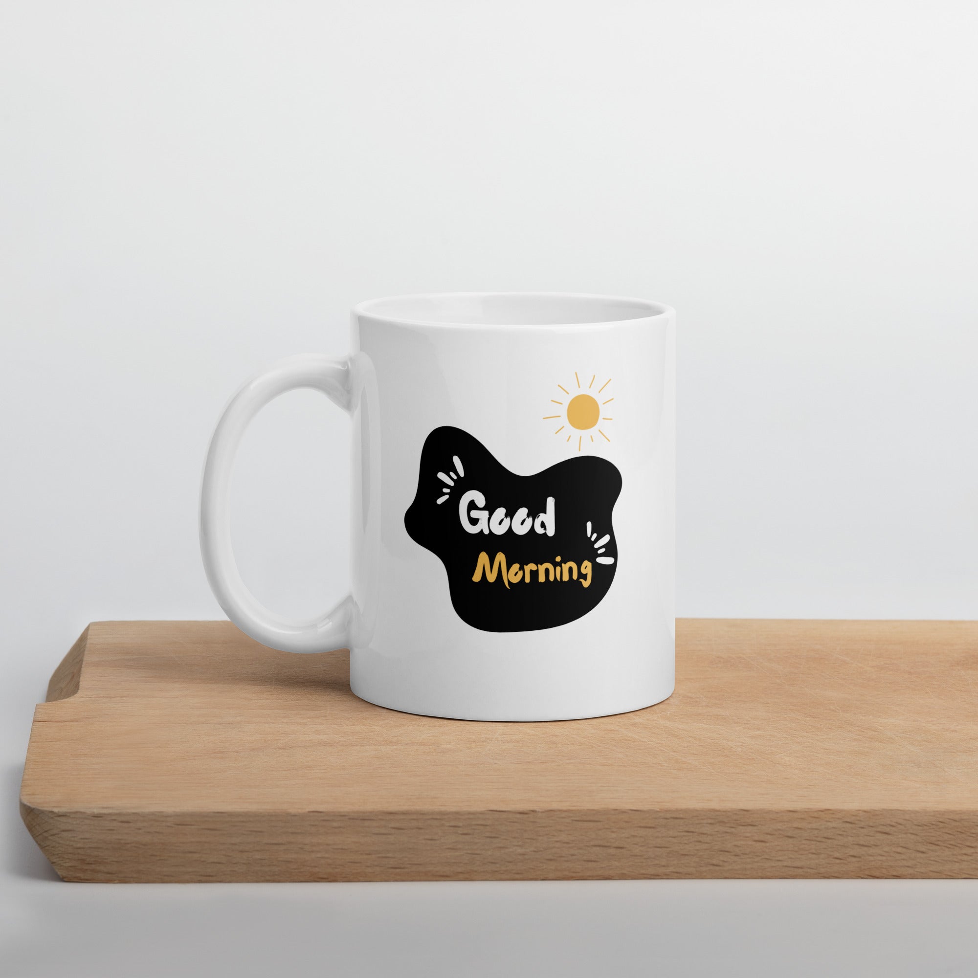 A glossy white ceramic mug with a mountain path design and a text 'GOOD MORNING' on the other side, placed against a plain background.