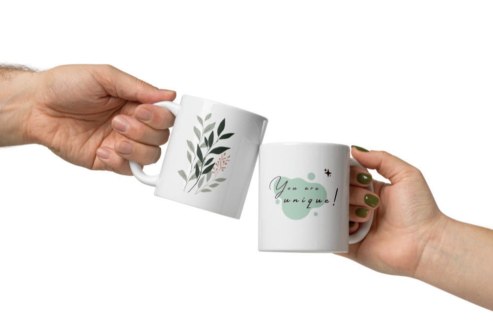 Two hands holding white mugs with decorative designs on a white background