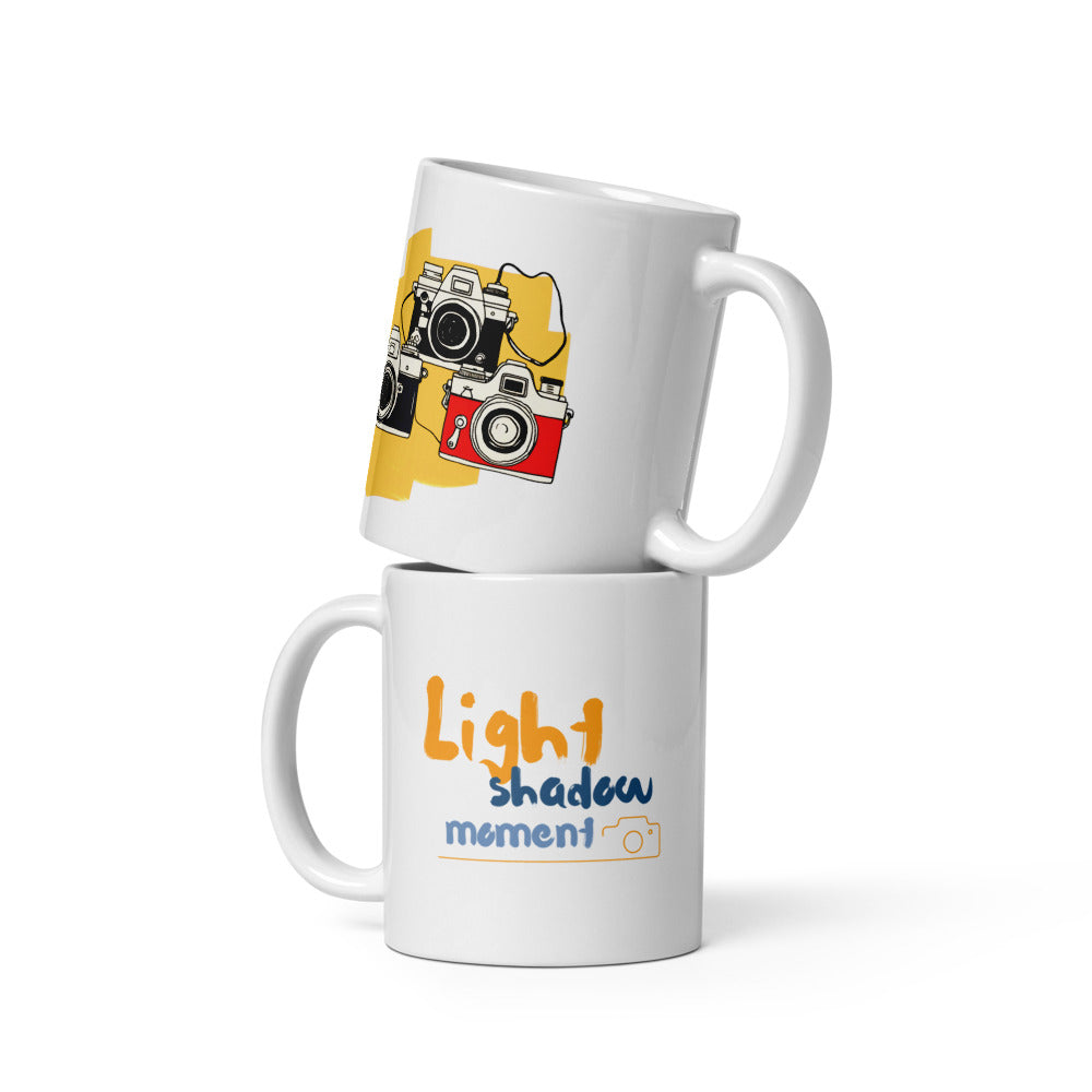 Two ceramic mugs, one with a colorful retro camera collage design and the text 'Light, Shadow, Moment!' The other mug is plain white with no design.