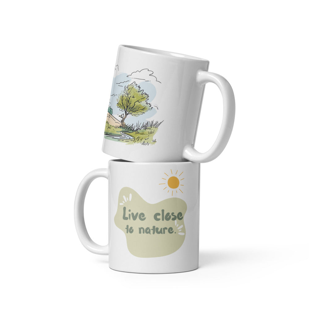 Two white ceramic mugs with a green and brown tree illustration and the quote 'Live Close to Nature'. One mug shows the exterior while the other displays the interior with a beverage.