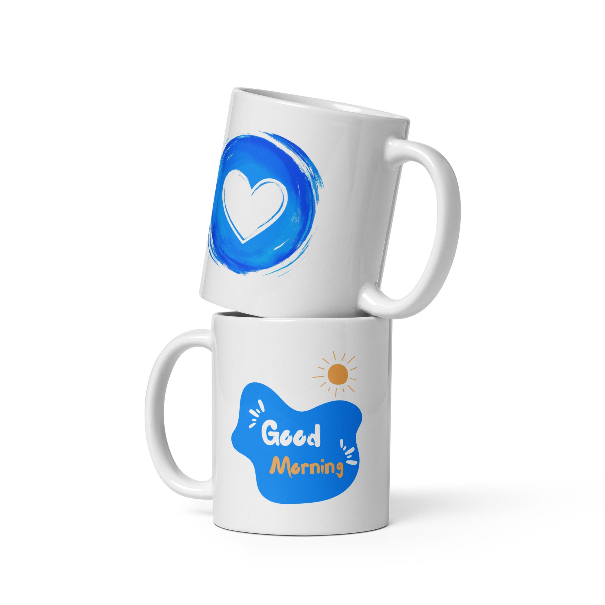 Two ceramic coffee mugs, one with a blue heart design and the other with a 'Good Morning' message alongside a sun icon, both with white backgrounds.
