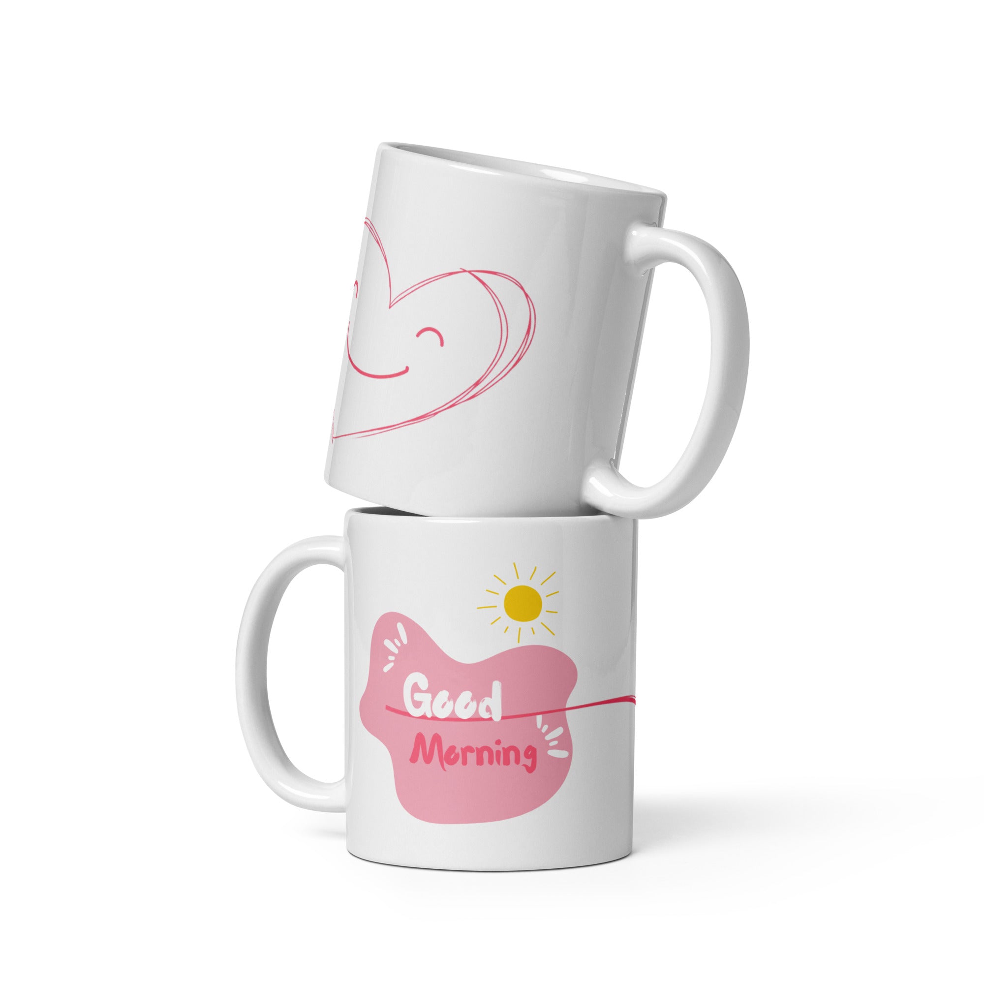Two ceramic coffee mugs, one with a smiling heart design on the front and the other with a 'Good Morning' message alongside a sun graphic on the front. Both mugs have a white background with text and heart illustrations.