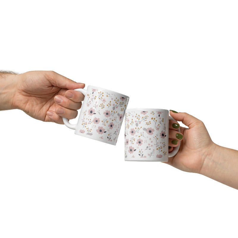 Two ceramic coffee mugs with a floral pattern, one with the handle up and the other with the handle down, on a white background.