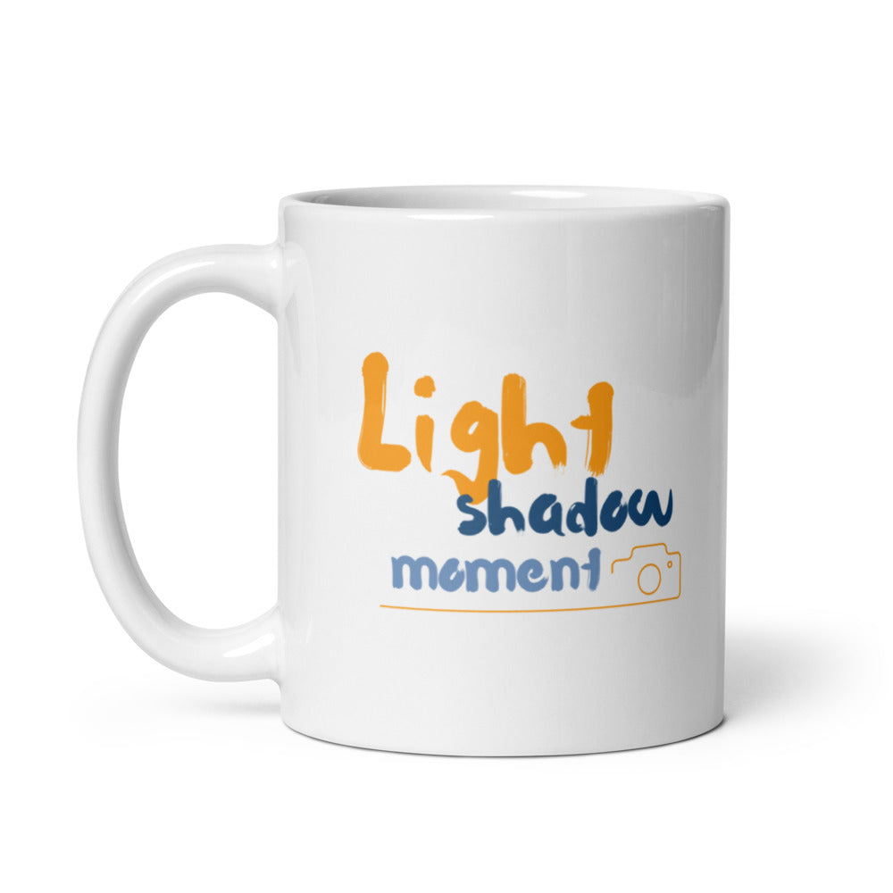 Two ceramic mugs, one with a colorful retro camera collage design and the text 'Light, Shadow, Moment!' The other mug is plain white with no design.
