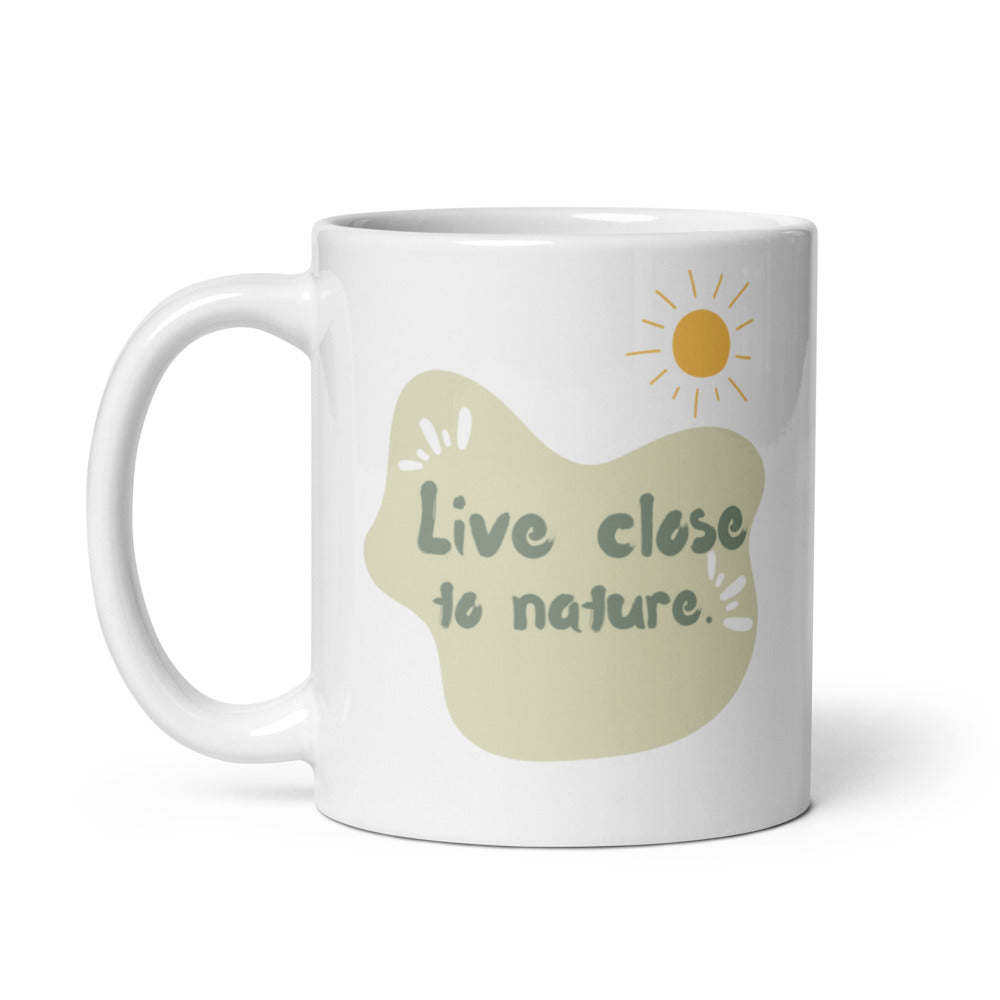 Two white ceramic mugs with a green and brown tree illustration and the quote 'Live Close to Nature'. One mug shows the exterior while the other displays the interior with a beverage.