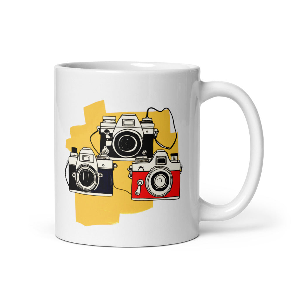 Two ceramic mugs, one with a colorful retro camera collage design and the text 'Light, Shadow, Moment!' The other mug is plain white with no design.
